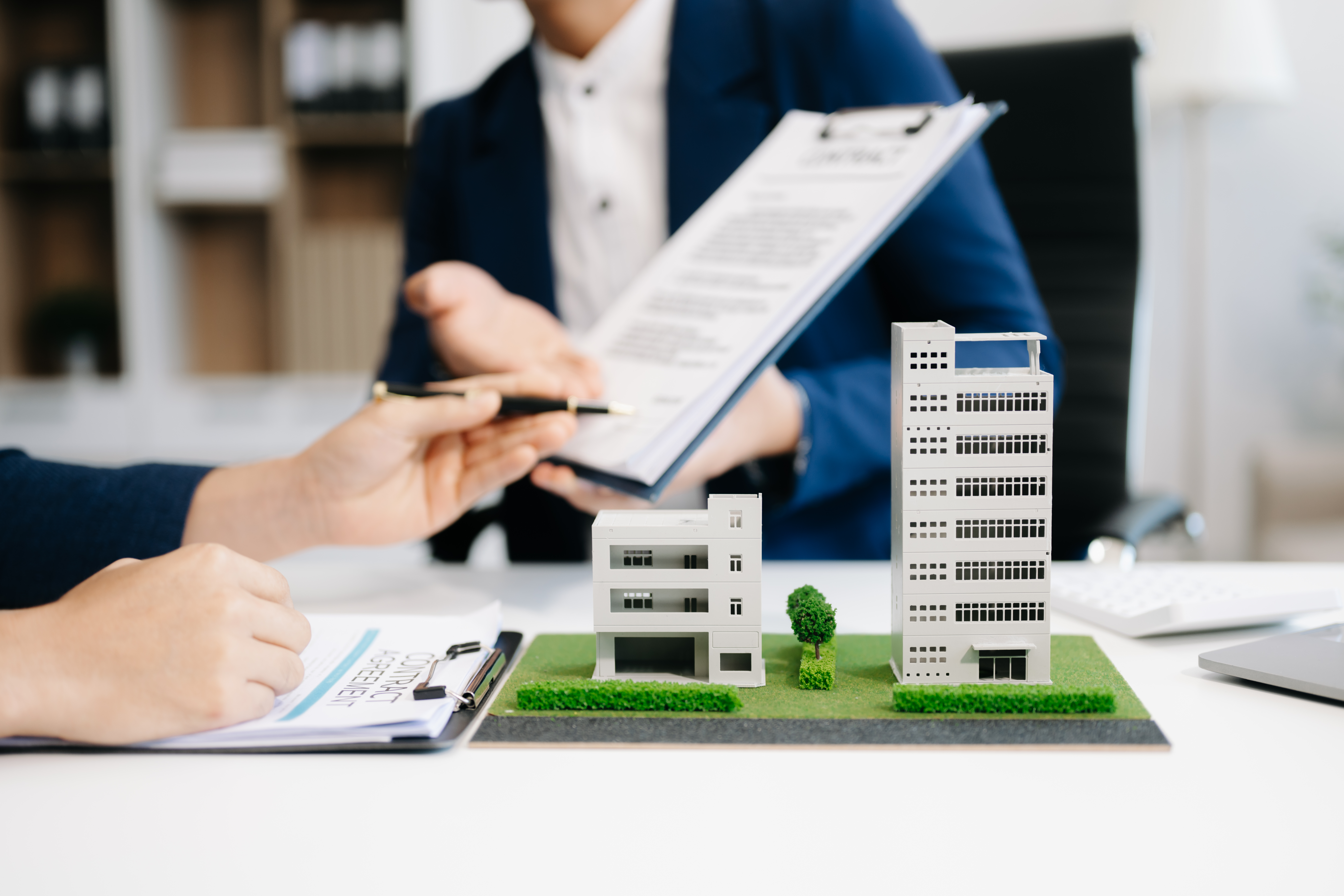Maqueta inmobiliaria: Manos revisando planos y documentos junto a una maqueta de edificios modernos.